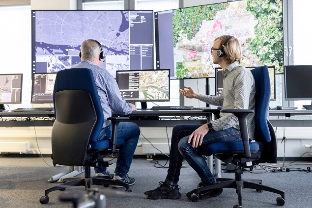 Zwei Mitarbeitende im Leitstand von HHLA Sky koordinieren über Monitore Drohnenflotten und Roboter weltweit in Echtzeit.