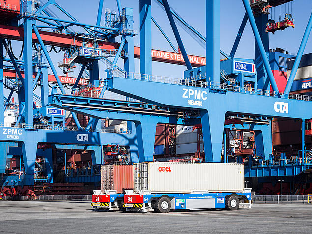 Two autonomous transport vehicles (AGVs) move containers beneath a container crane at the HHLA Container Terminal Altenwerder in Hamburg.