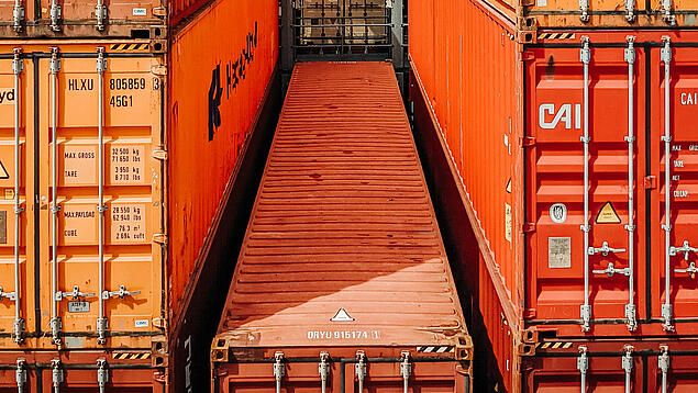 Mehrere orange- und braunfarbende Container aufeinandergestapelt.