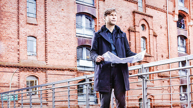 Kaufmännisches Immobilienmanagement bei der HHLA: Experte begutachtet Bestandsimmobilie in der Hamburger Speicherstadt mit Architekturplänen zur Budget- und Projektplanung.