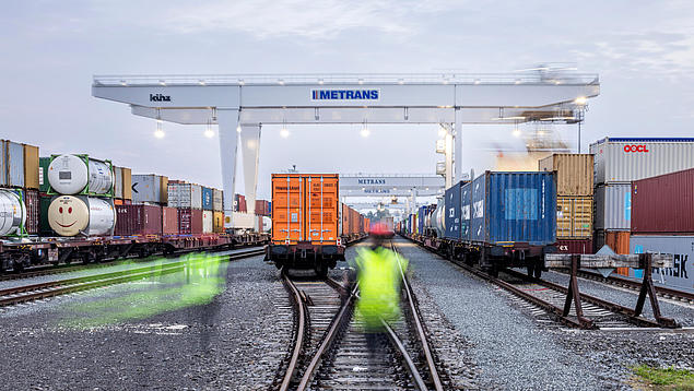 Metrans container terminal with rail crane, container trains and blurred staff – part of a high-performance intermodal rail network of HHLA in Europe.