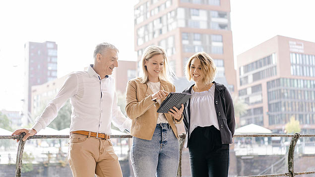 Drei Experten von HHLA Immobilien bei der Projektentwicklung im Gespräch vor modernen Bürogebäuden in der Hamburger HafenCity.